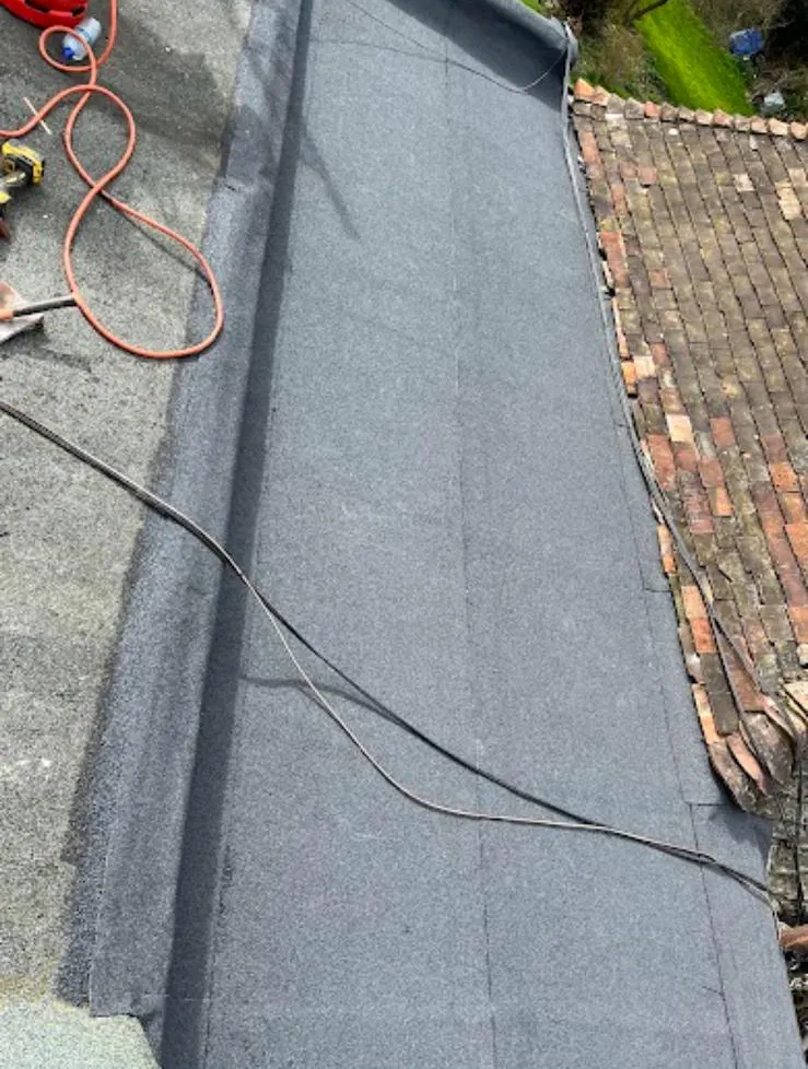 Grey mineral felt flat roof dressed against a tiled slope