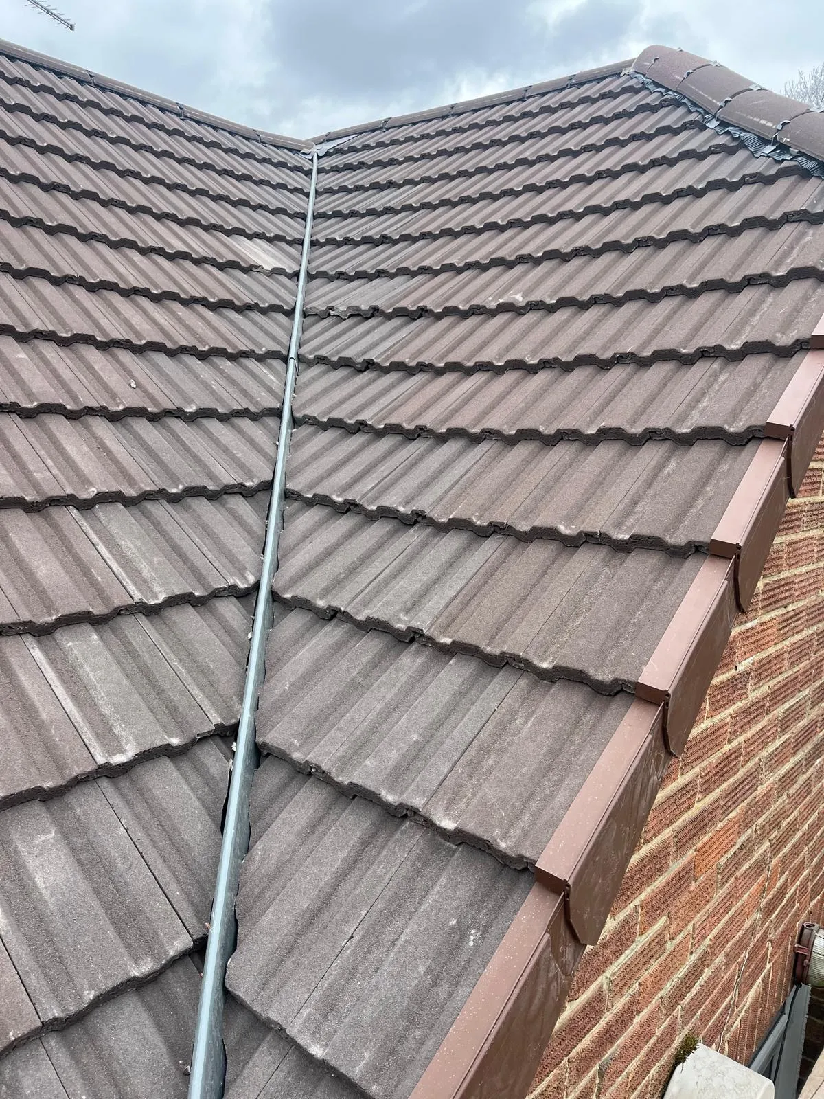 Finished brown tile roof meeting a brick gable