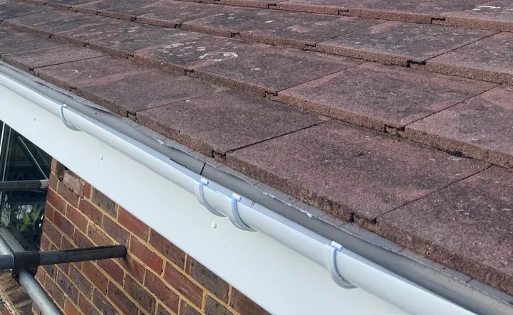 White fascia board and half-round gutter on its brackets, under the bottom row of tiles