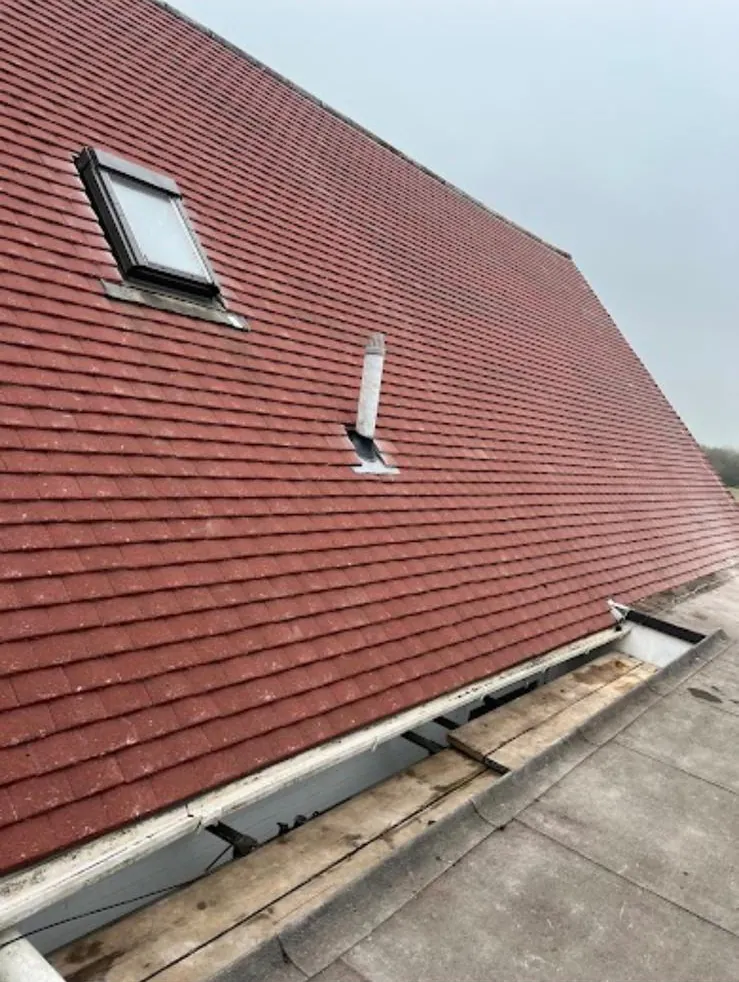Red plain tile roof with a roof window and a vent, fascia off at the eaves