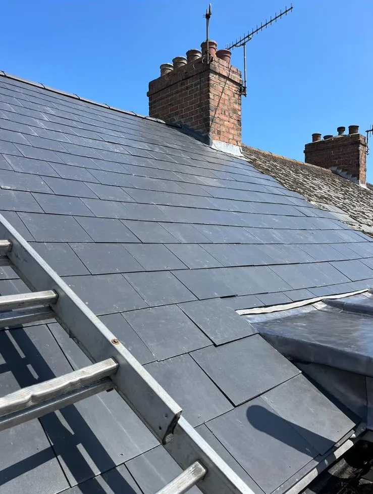 New grey slate roof laid around a brick chimney